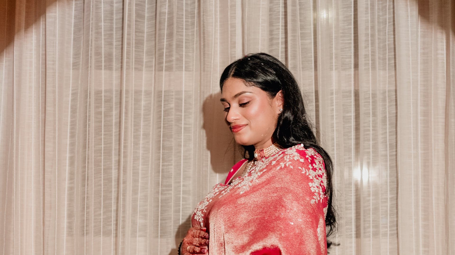 Sneha cradling her baby bump in her pink saree